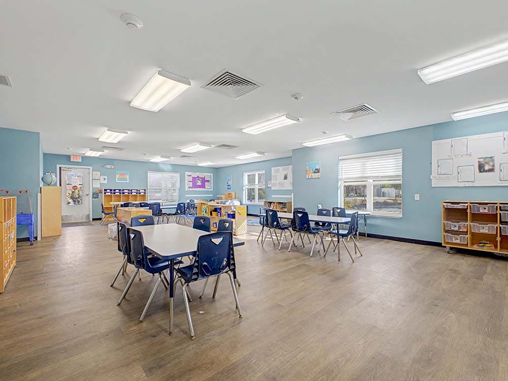 Empty classroom with small tables and chairs, and light blue walls