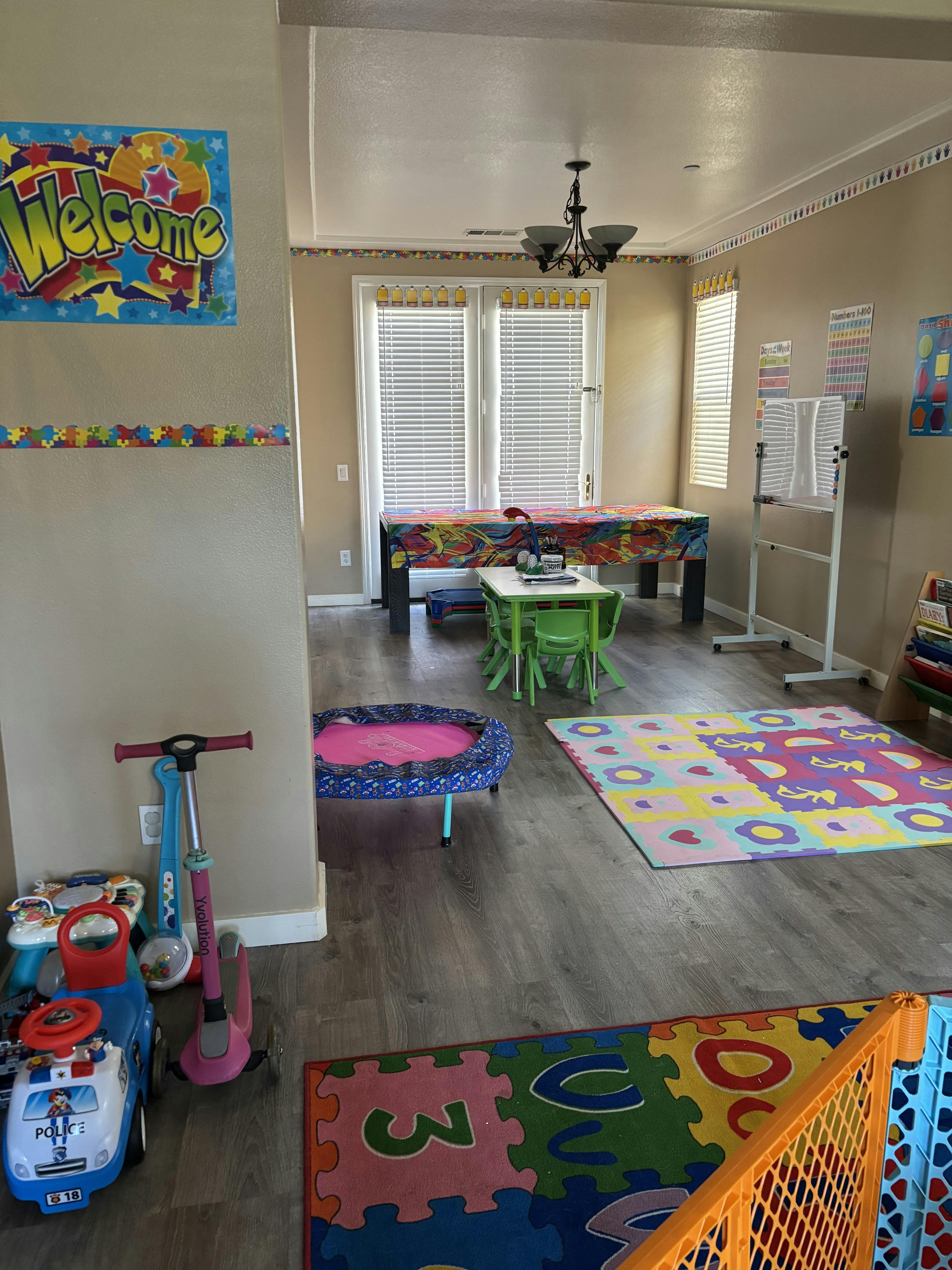 Child's playroom with a table and chairs, play mats, toys, and a "Welcome" sign