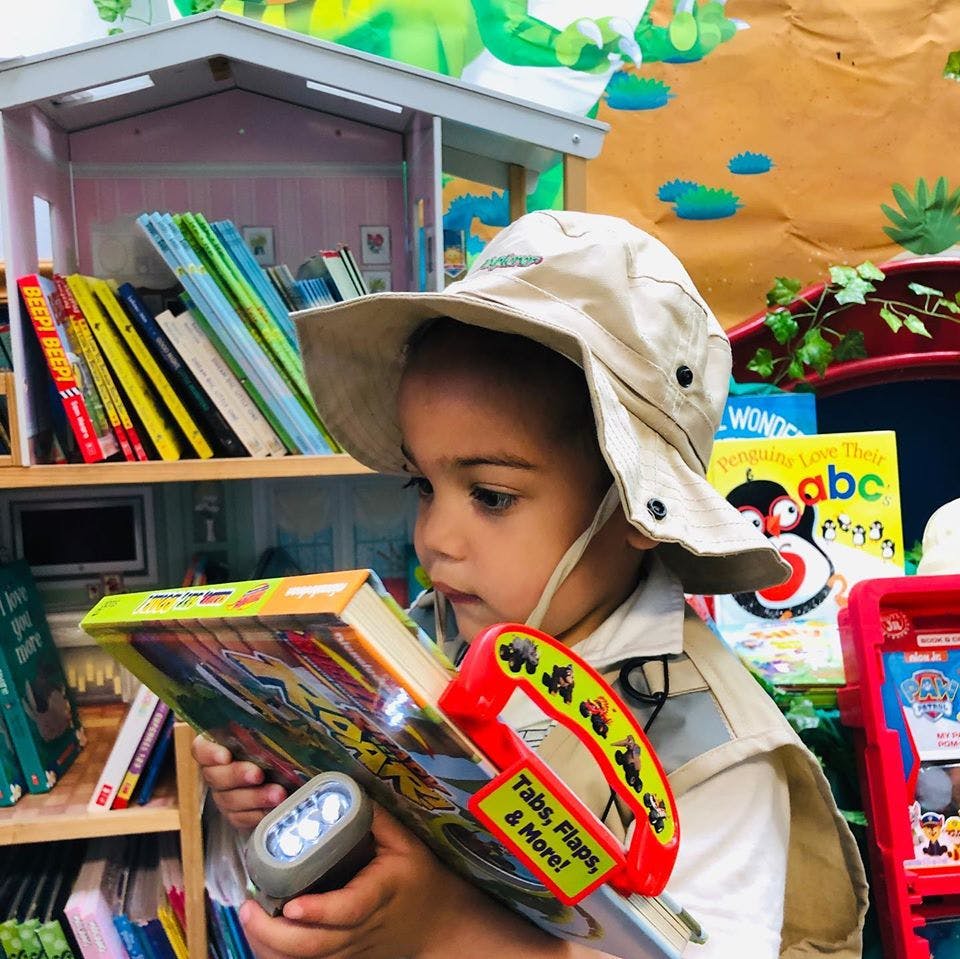Child in a hat holding a book and a flashlight