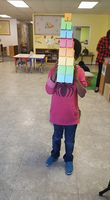 Child holding a tall stack of colorful blocks in a classroom