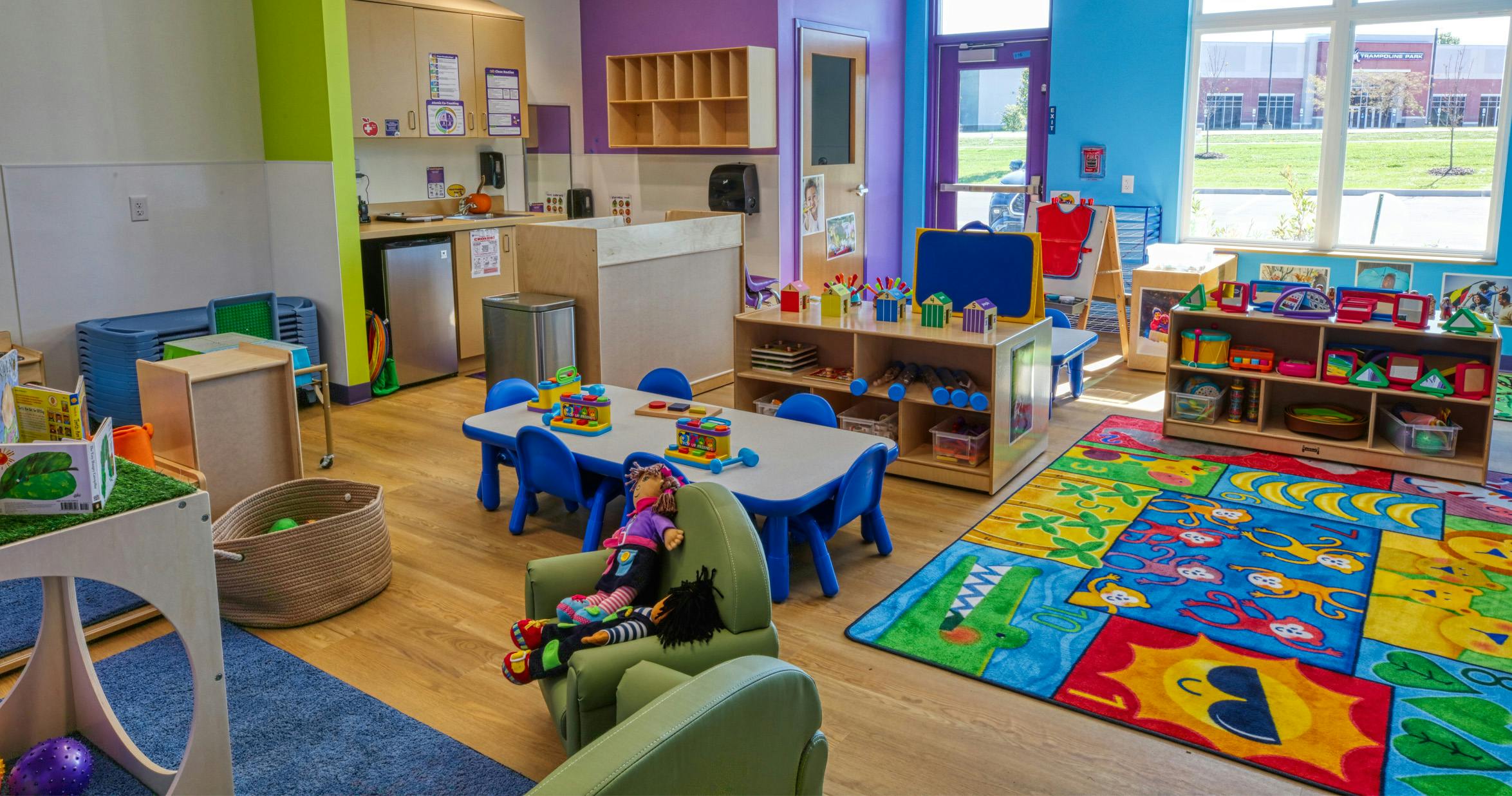 An empty colorful classroom with tables and chairs, toys, and a play rug