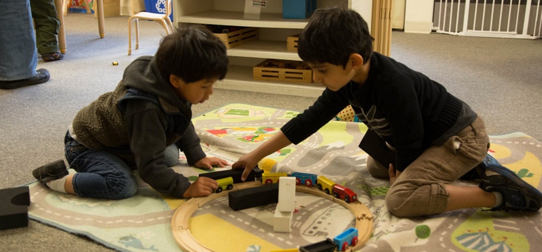 Two children playing with a toy train set on a rug