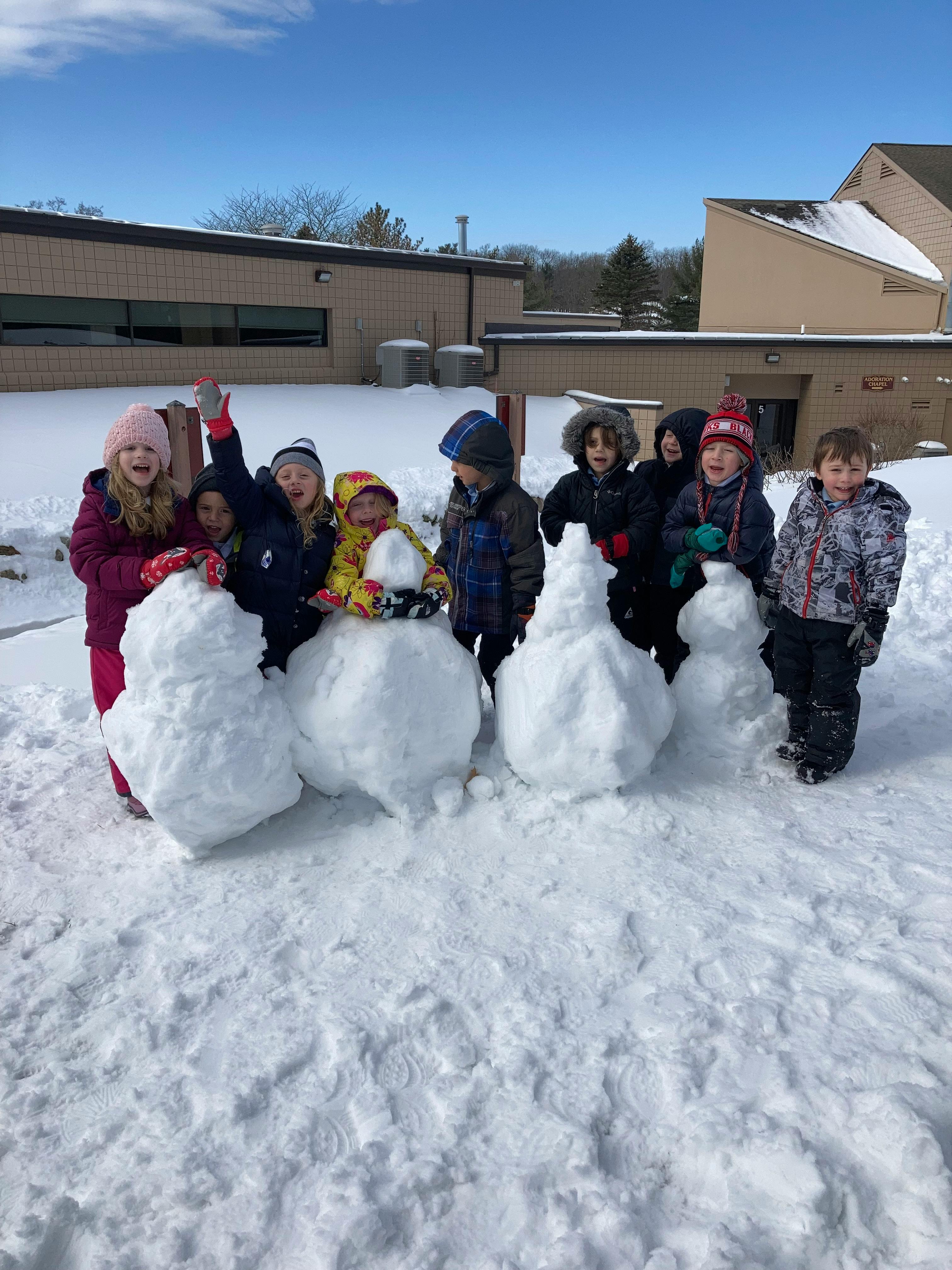 Group of children standing with snowmen in a snowy outdoor area