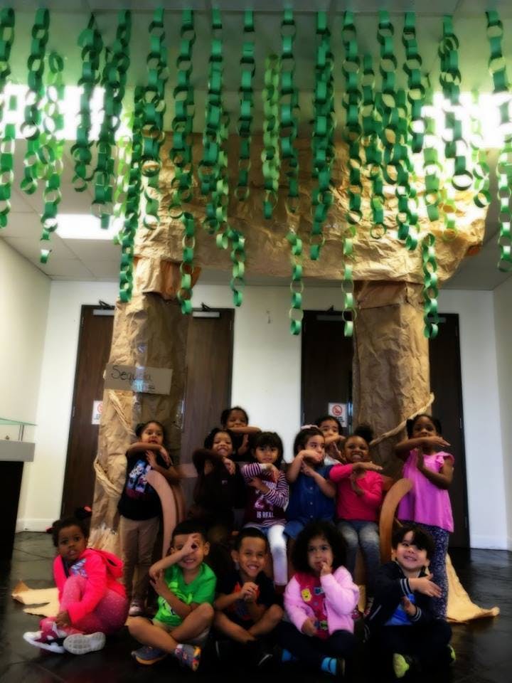 Children posing in front of a large paper tree with green paper chains hanging