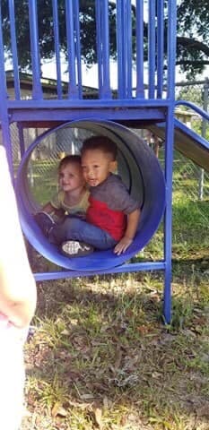 Two children sitting inside a blue tunnel on a playground