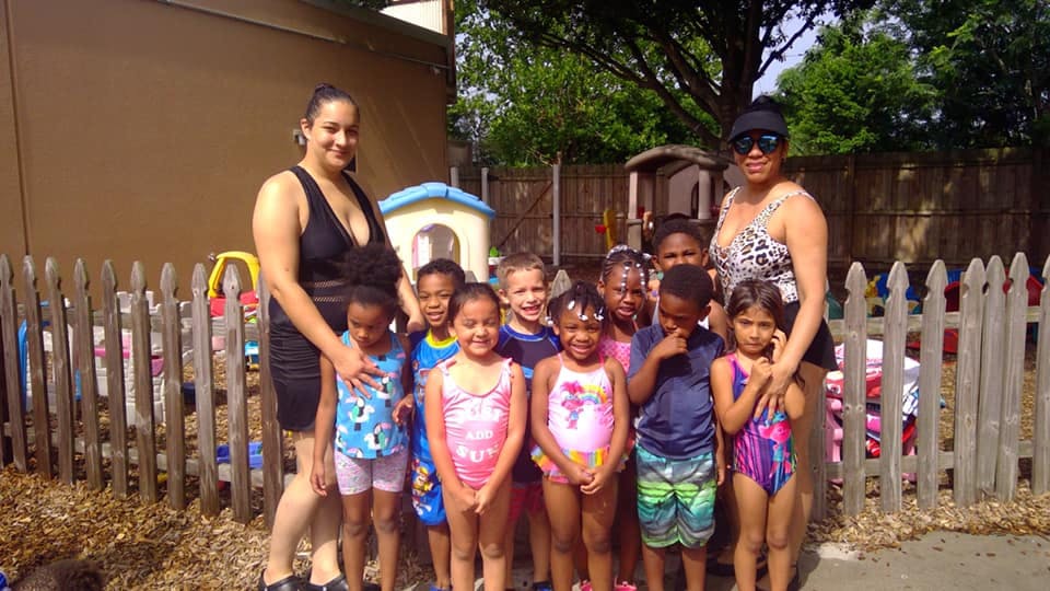 Two people with a group of children in swimsuits standing in front of a fence