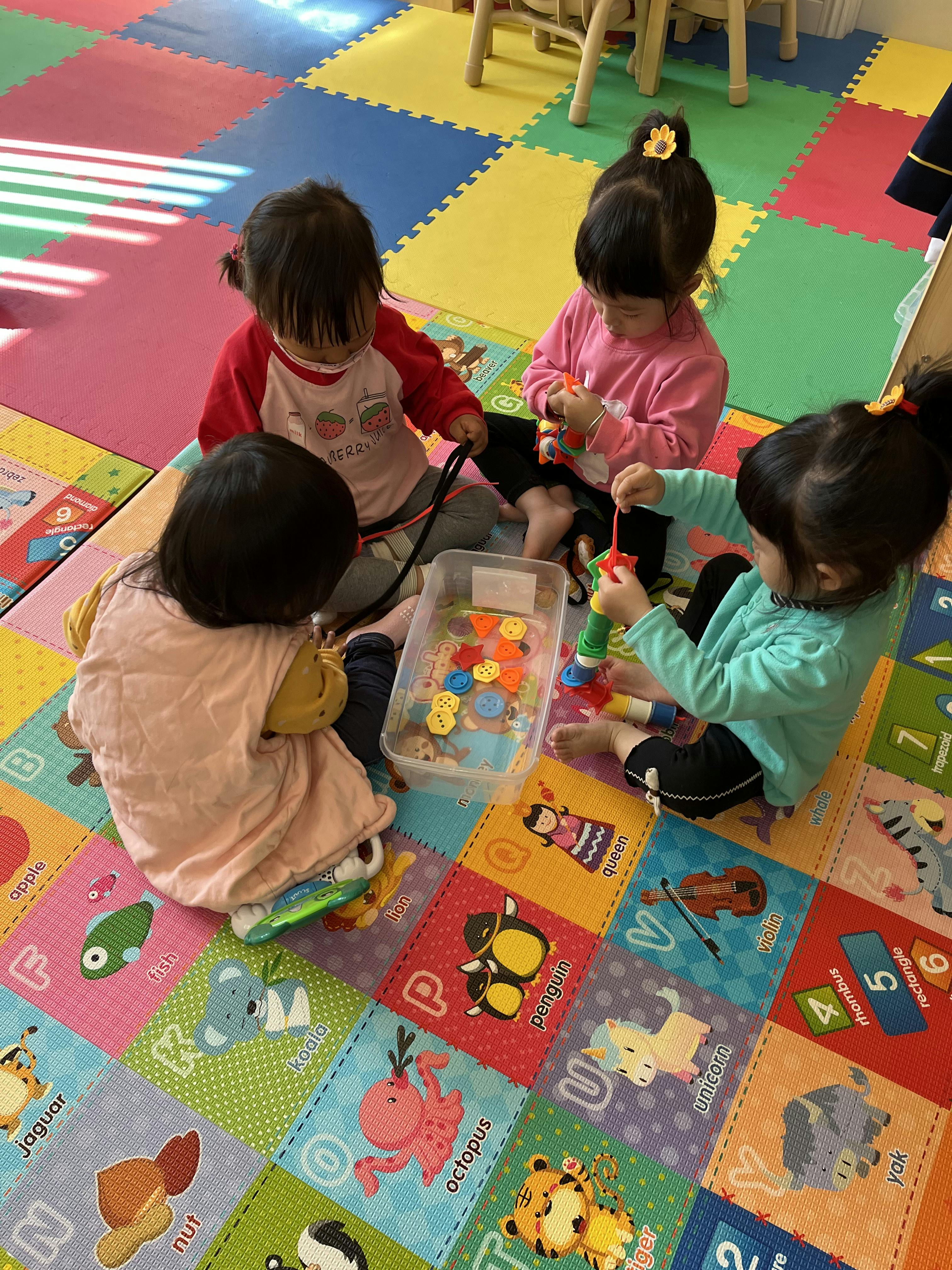 Four children playing with toys on a colorful mat