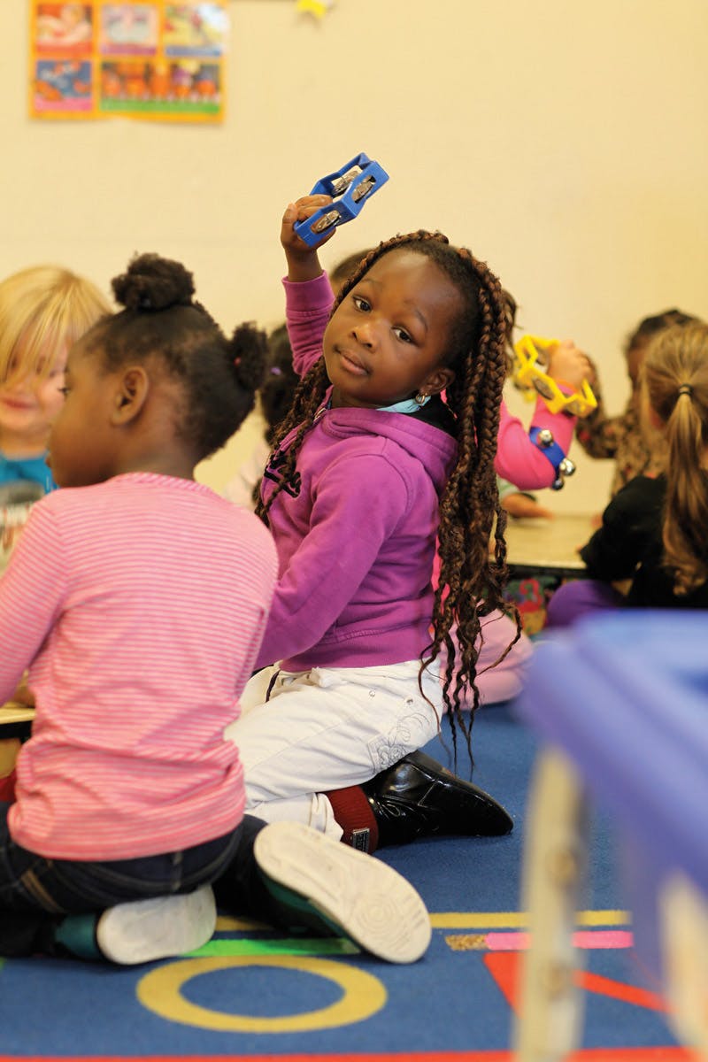 Child holding up a blue musical instrument in a classroom