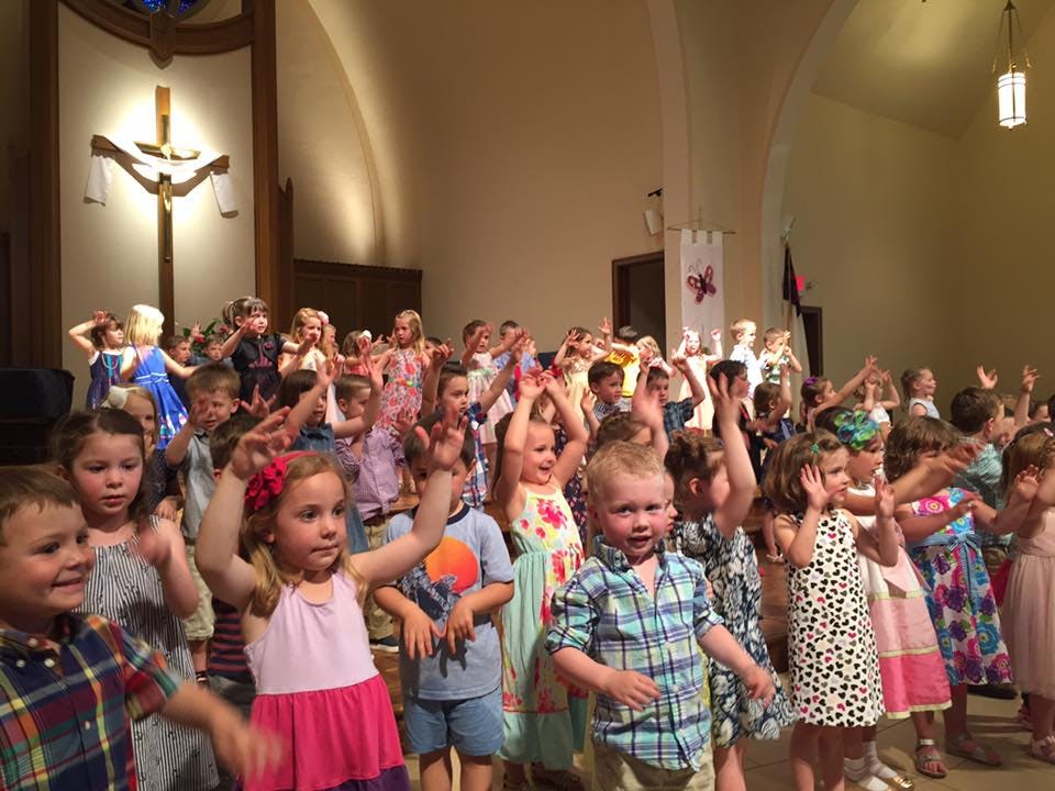 Group of children with hands raised in a large room