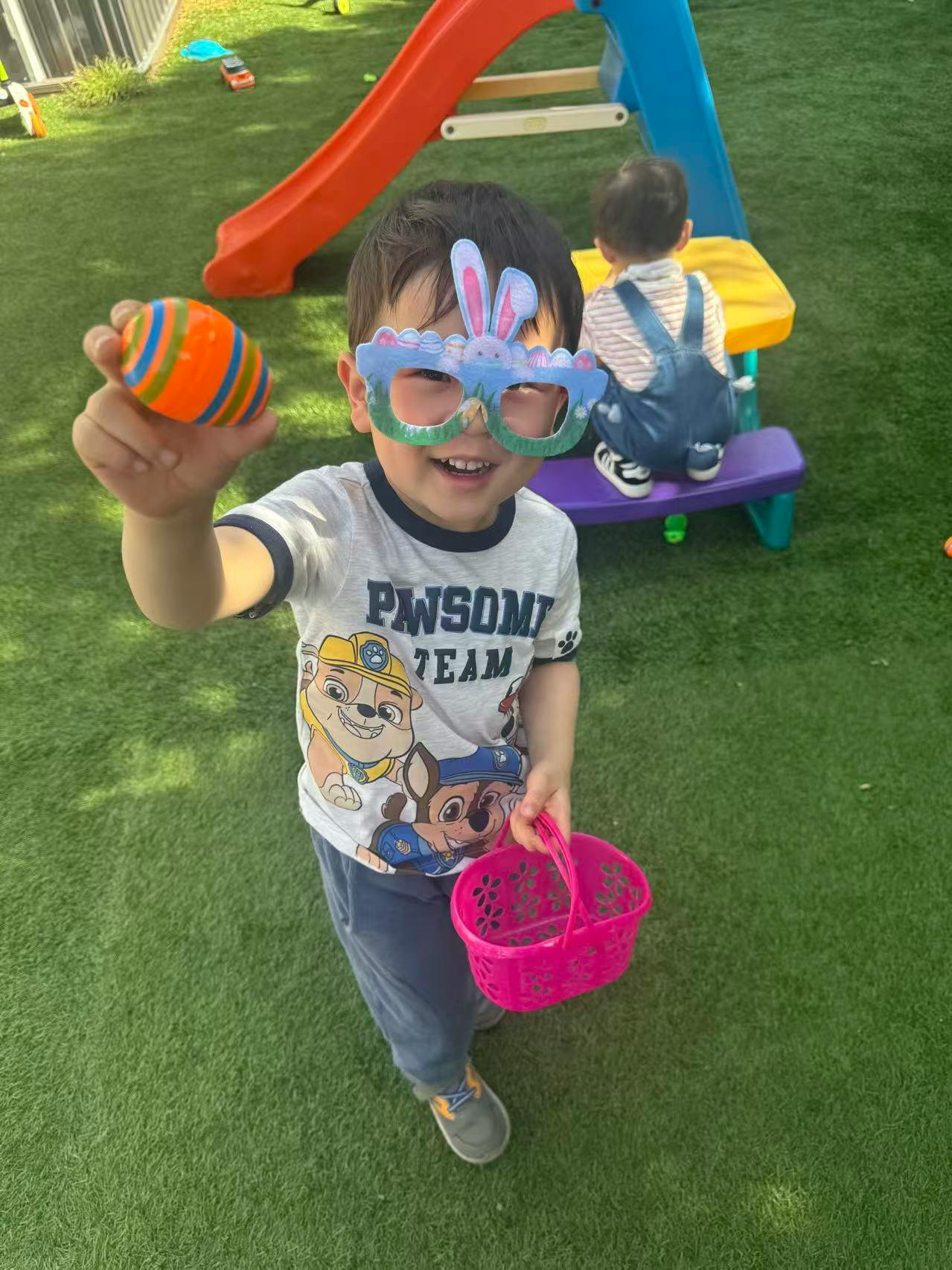 Child wearing bunny glasses and holding an orange striped egg and pink basket