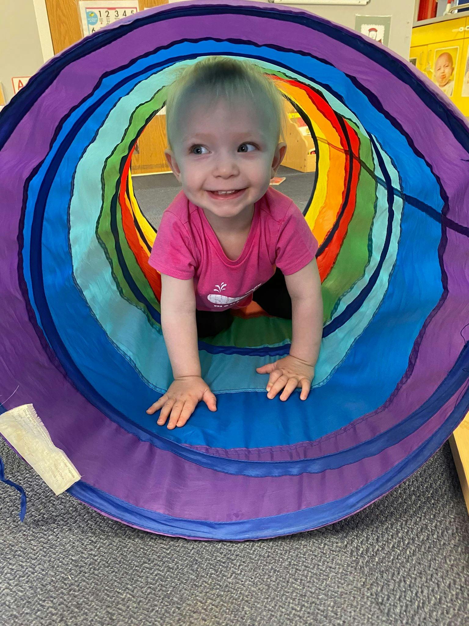 Child crawling through a colorful play tunnel
