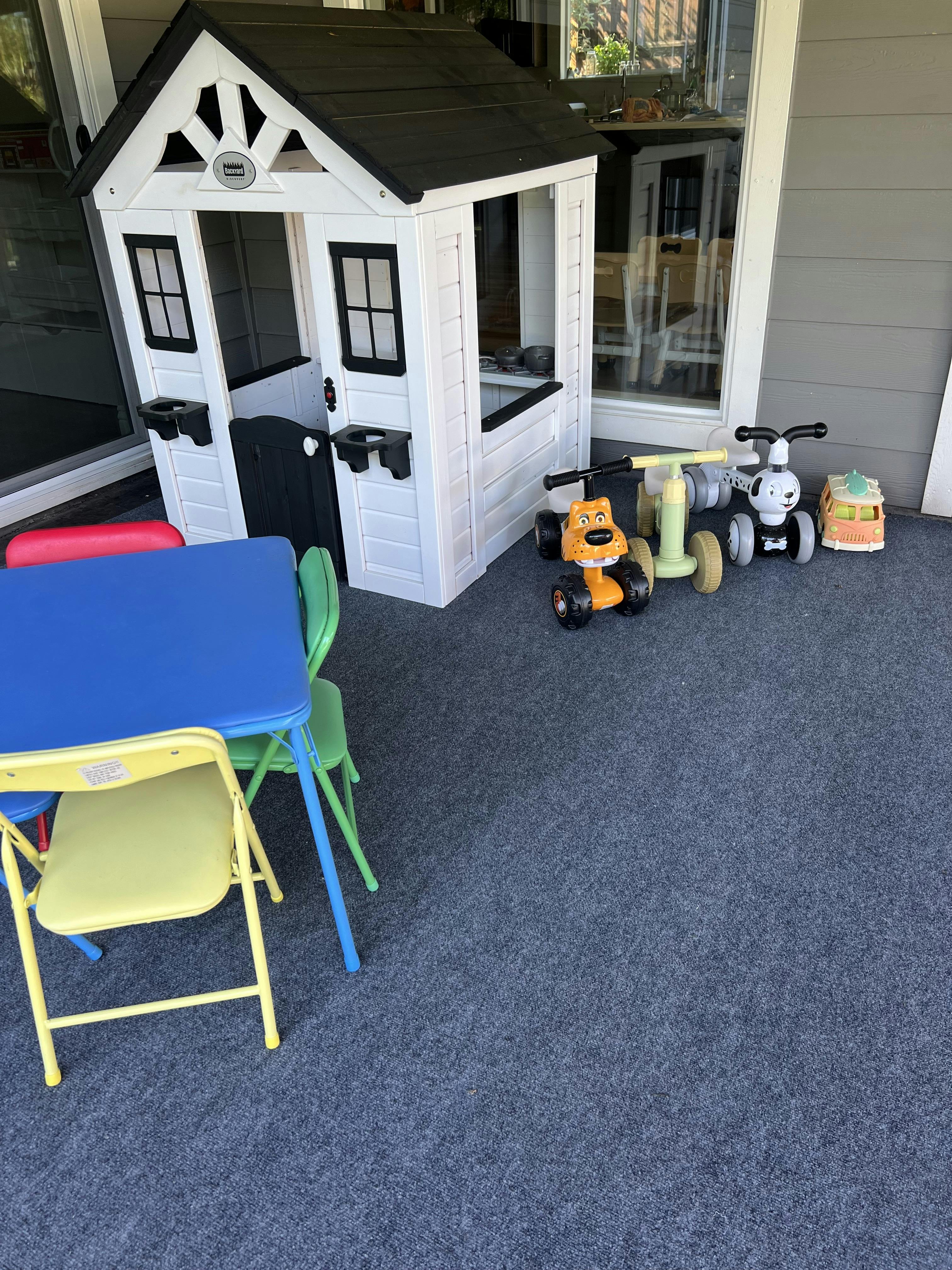 Children's playhouse, table with chairs, and ride-on toys on a carpeted patio