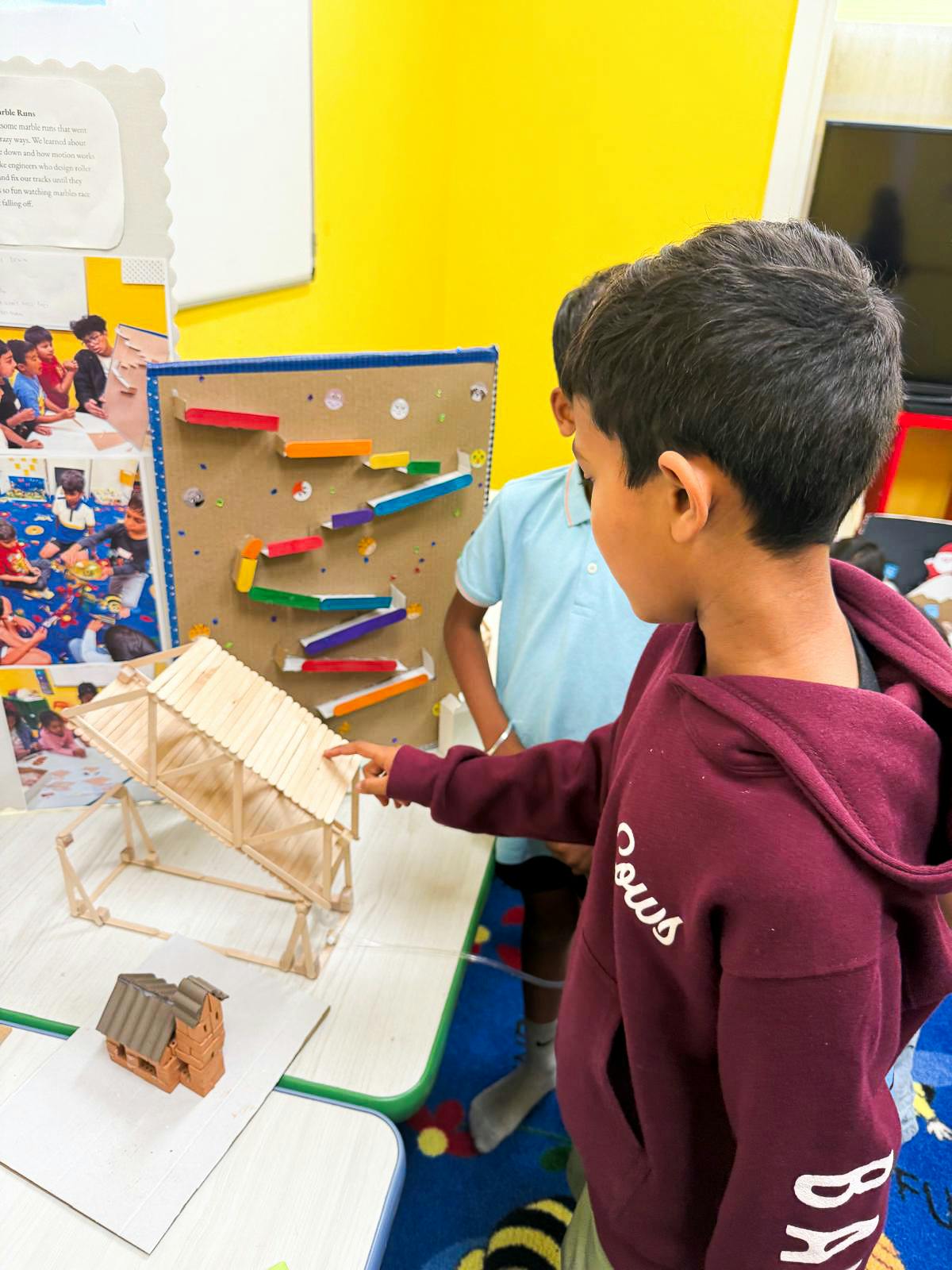 Child pointing at a wooden ramp next to a marble run