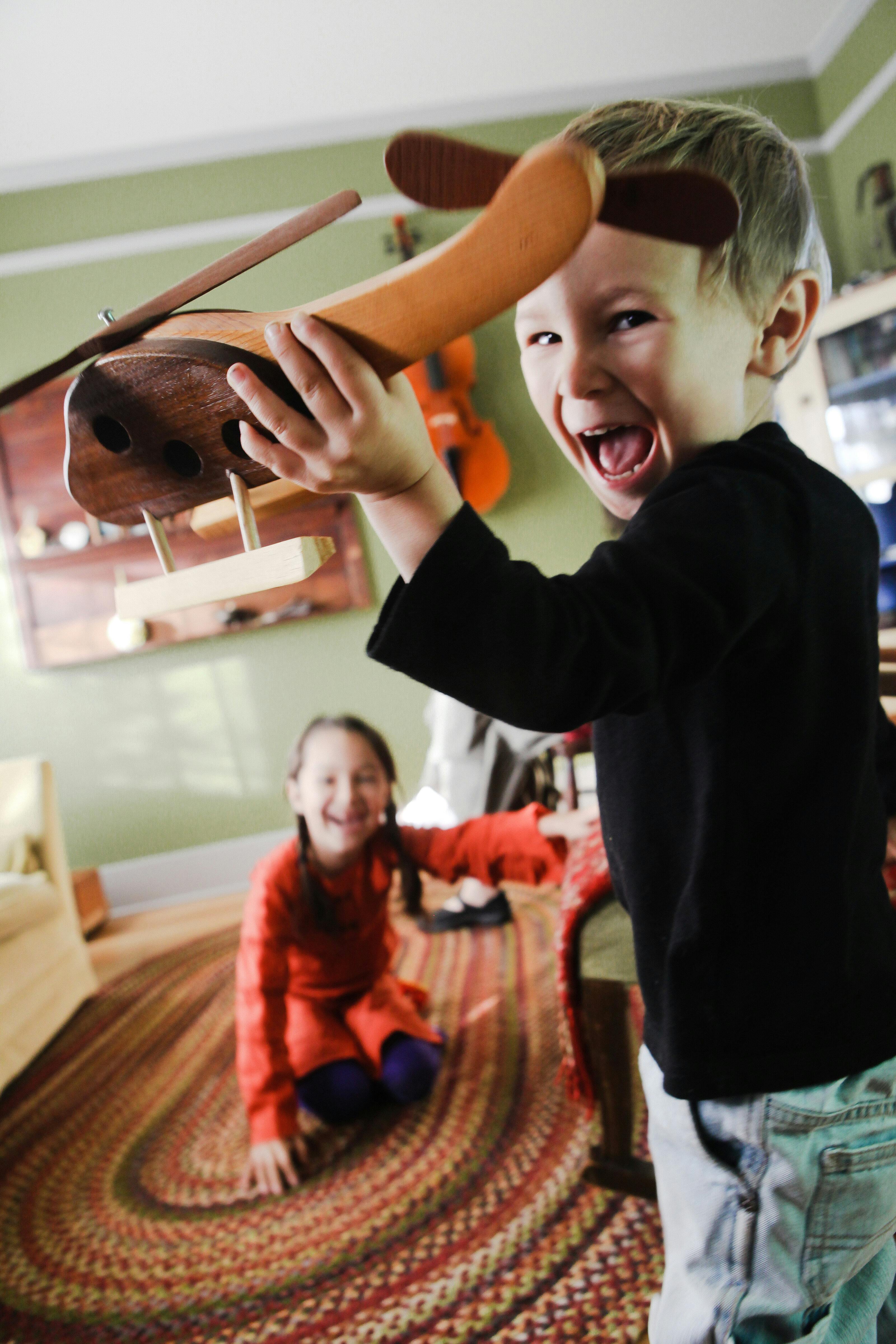 Child holding up a wooden toy airplane, another child in background