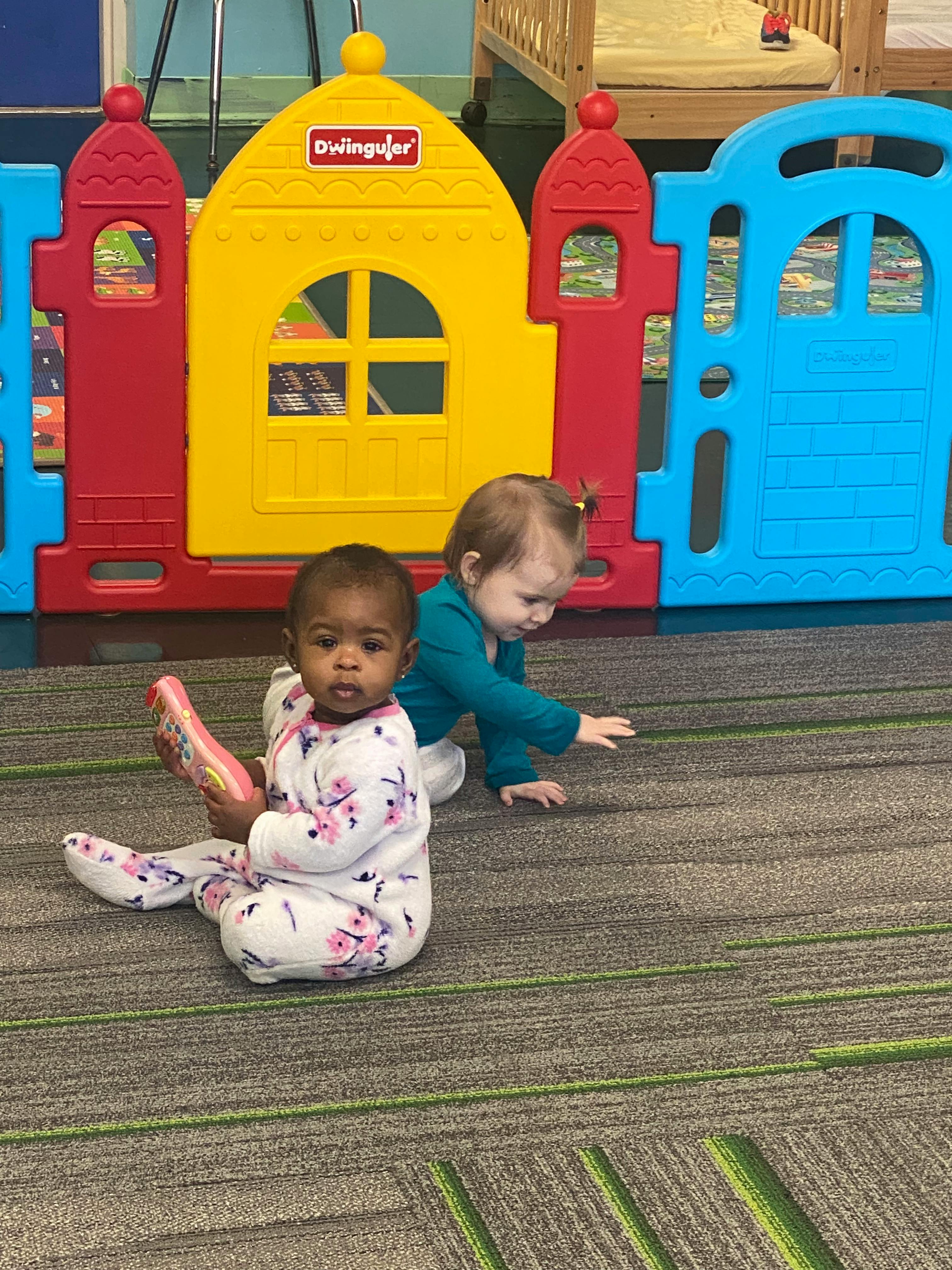 Two children on a carpeted floor with a playhouse in the background