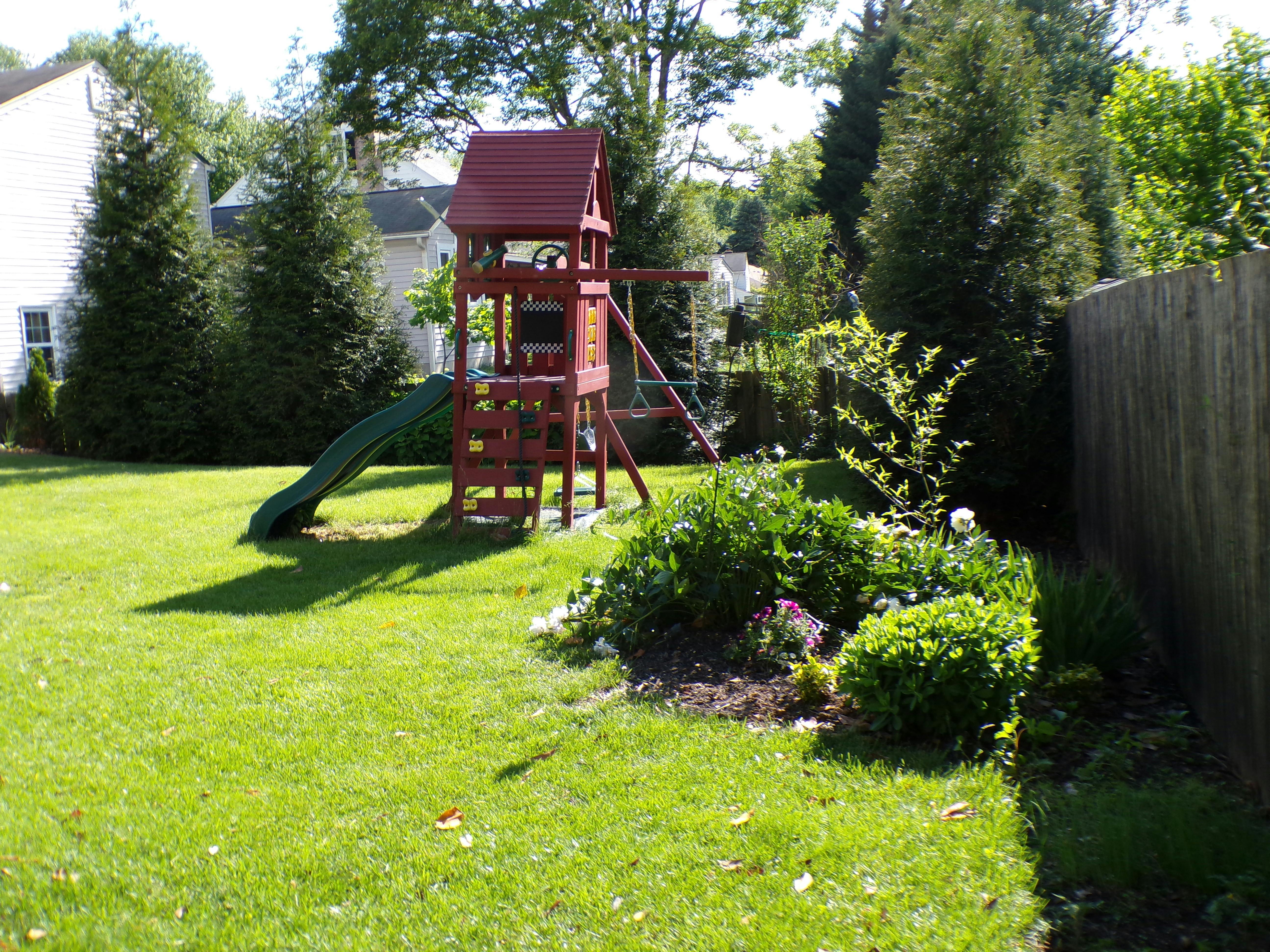 Wooden playset with a slide and swings in a grassy backyard