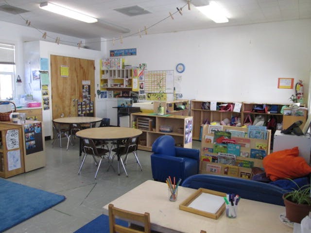 Classroom with small tables and chairs, shelves with books and supplies