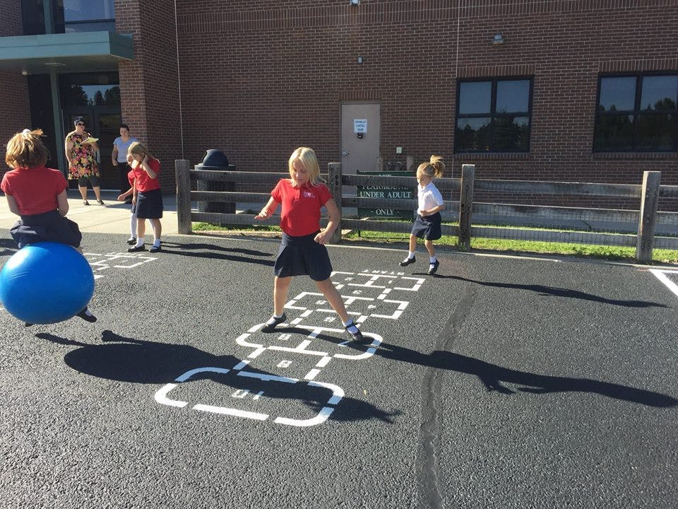 Children playing hopscotch and bouncing on a blue ball outdoors
