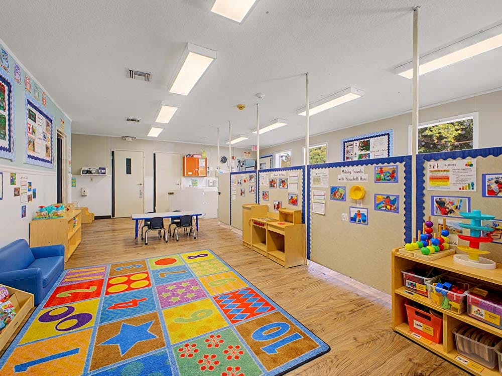 Children's classroom with colorful rug, blue couch, tables, and learning displays