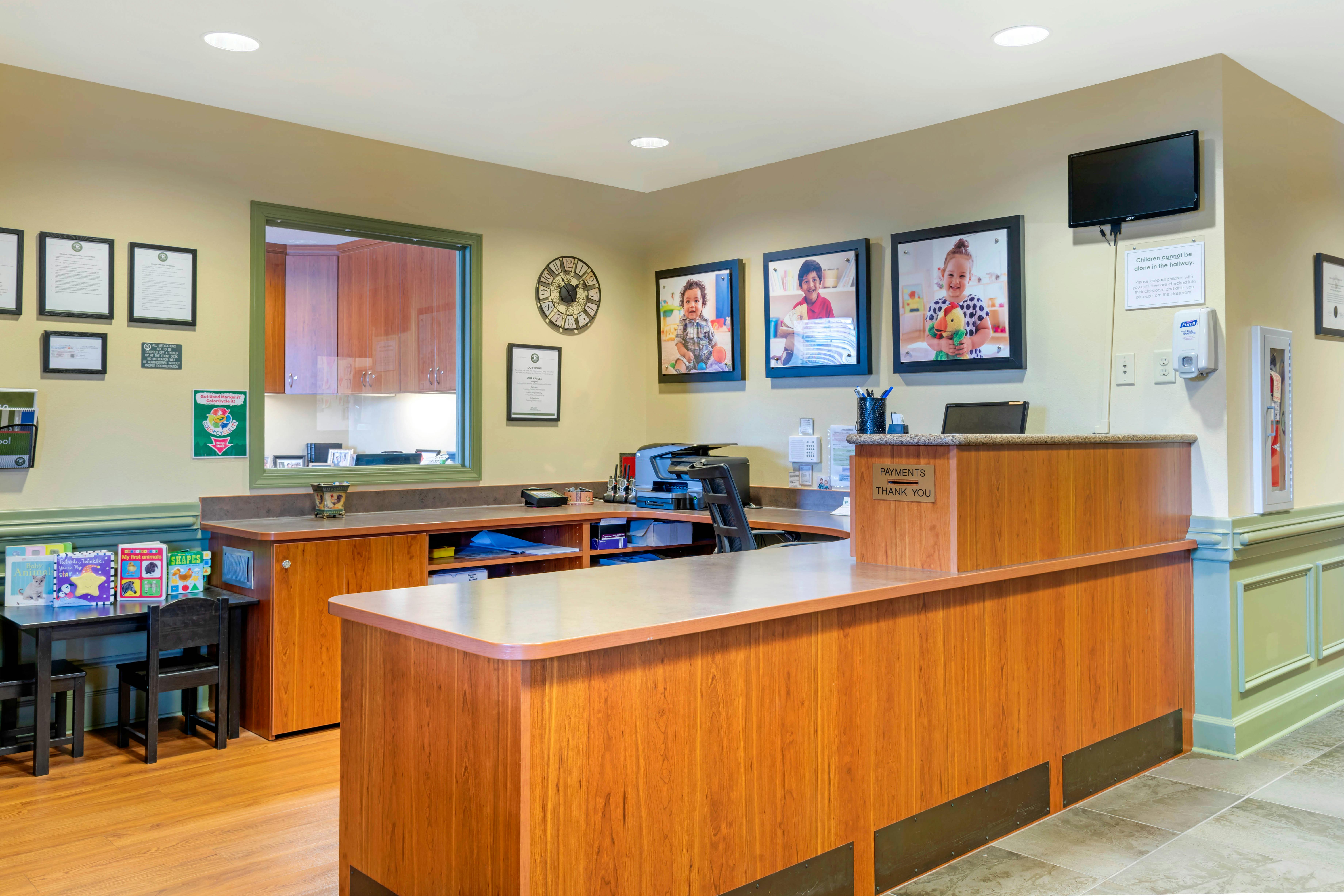 Reception desk with three framed photos of children above it, small children's table