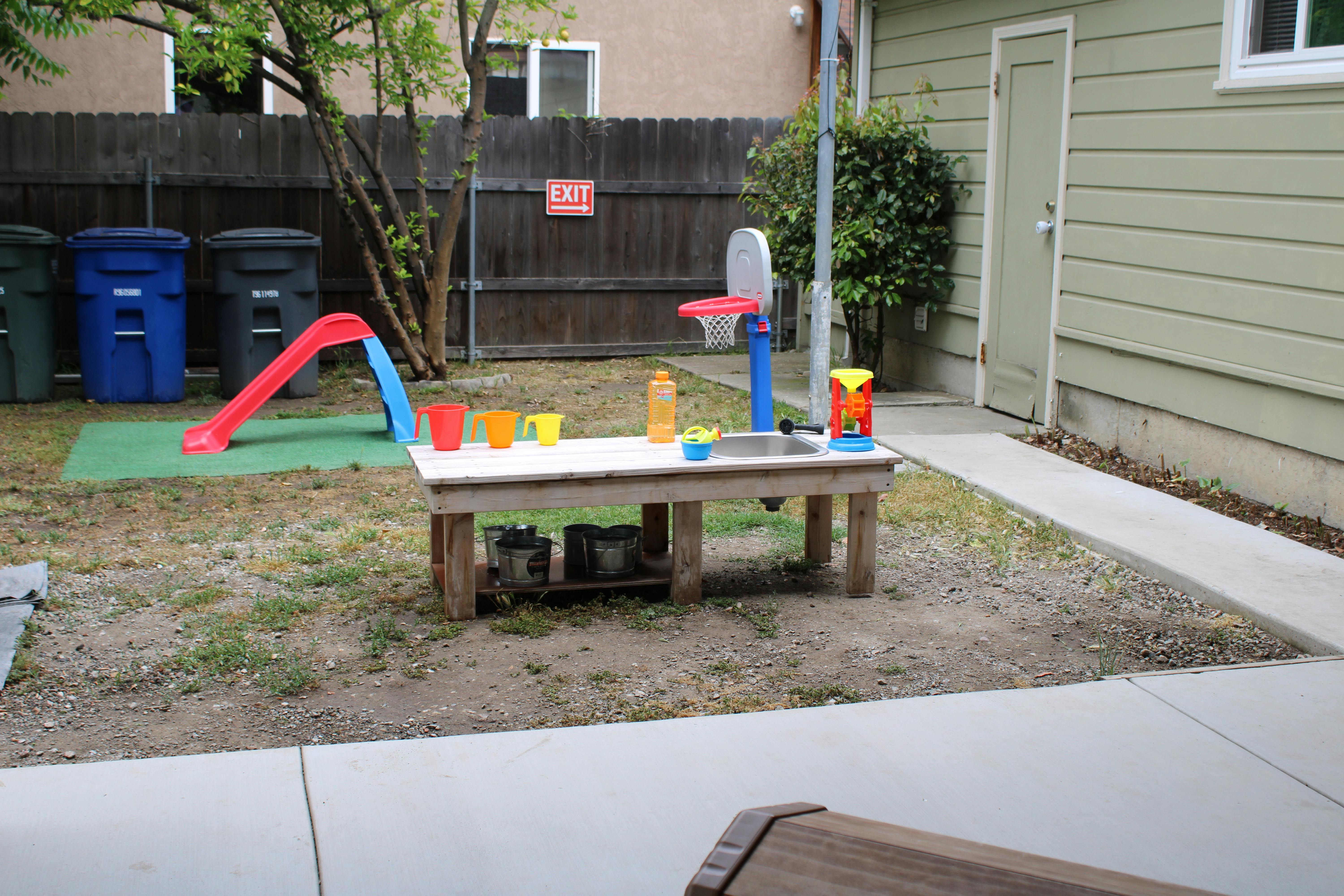 Backyard with a small slide, play table, and basketball hoop