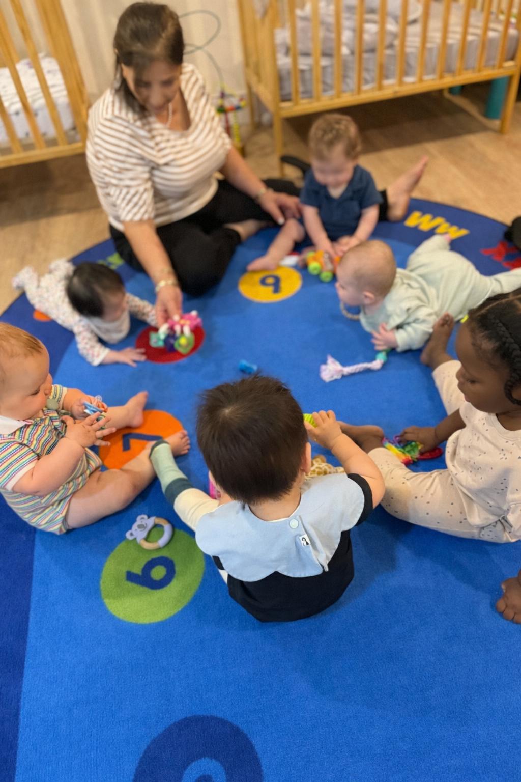 Adult and multiple children playing with toys on a blue mat