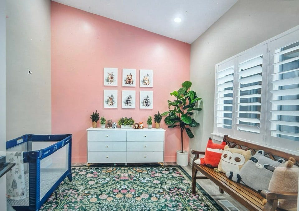Nursery room with a crib, dresser, and bench with a pink accent wall