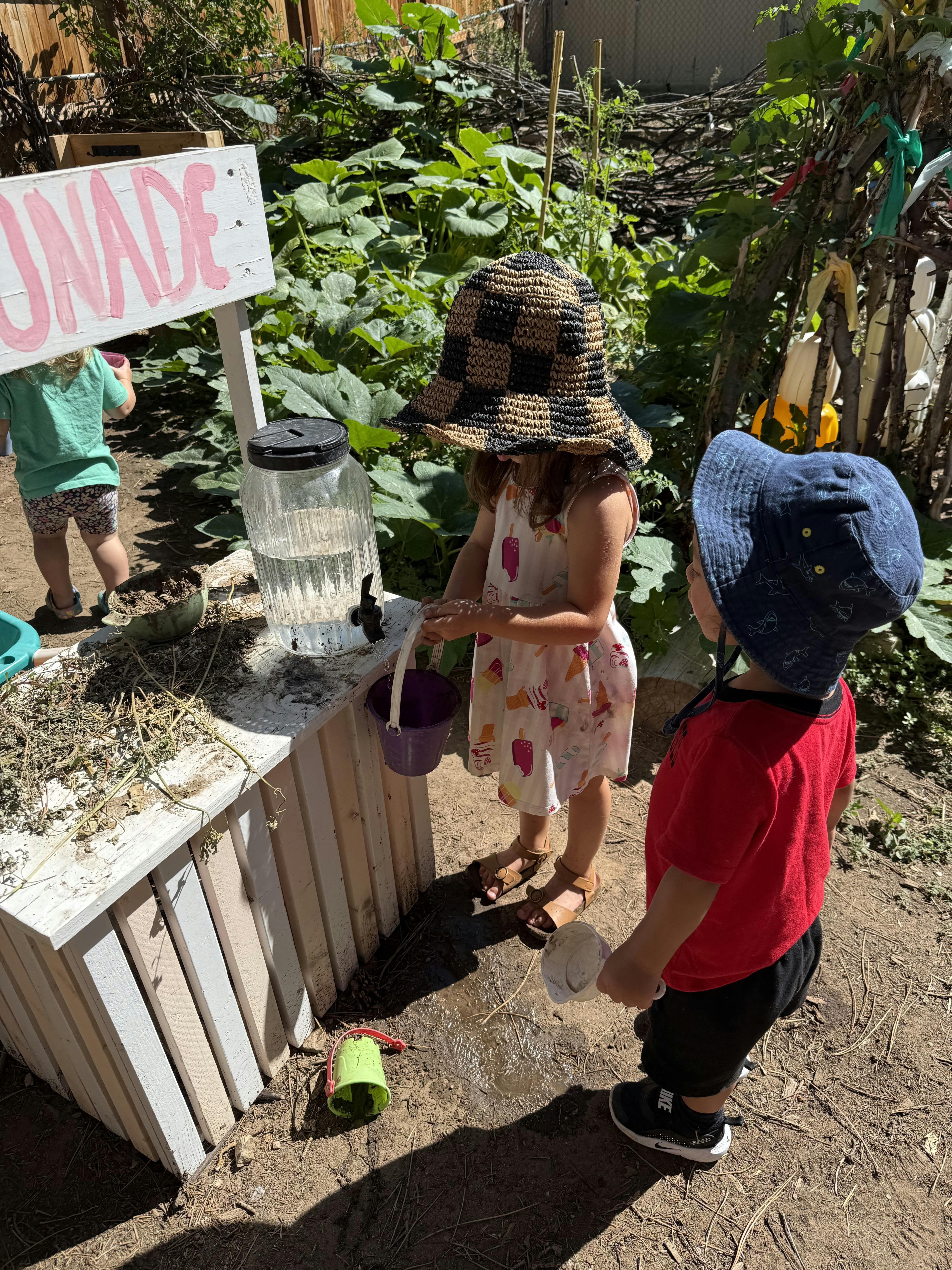 Children playing with a water dispenser at a lemonade stand in a garden