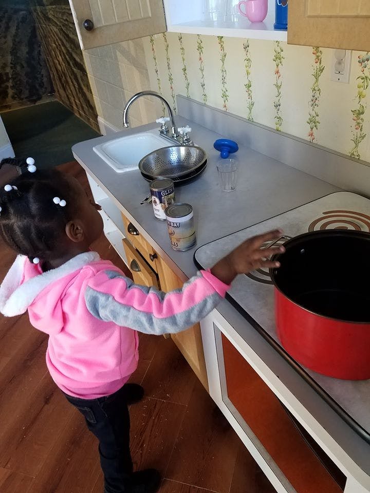 Child playing with a toy stove and pot in a play kitchen