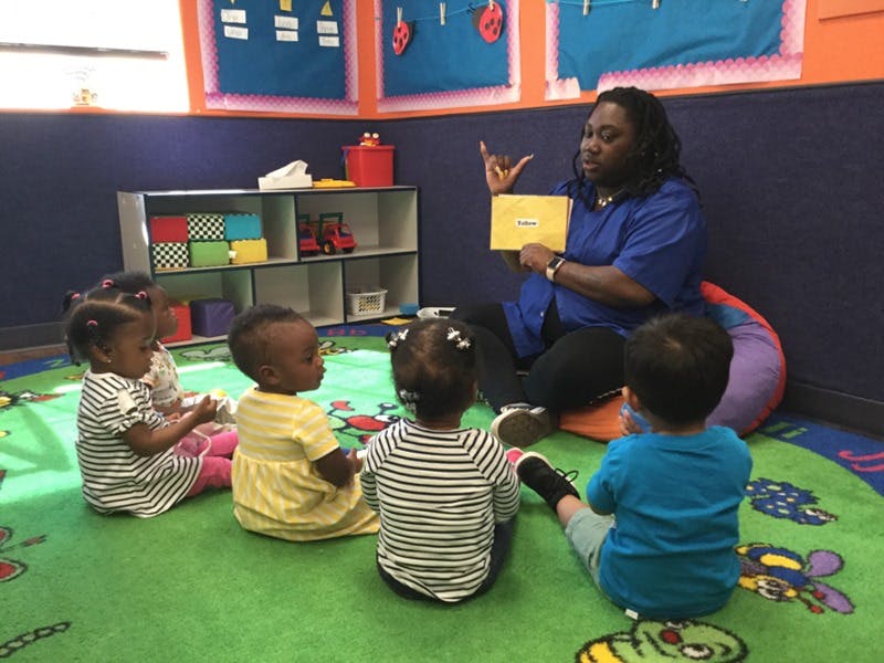 Adult holding a card and gesturing to children sitting on a rug in a classroom