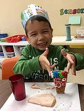 Child wearing a crown, making a craft at a table