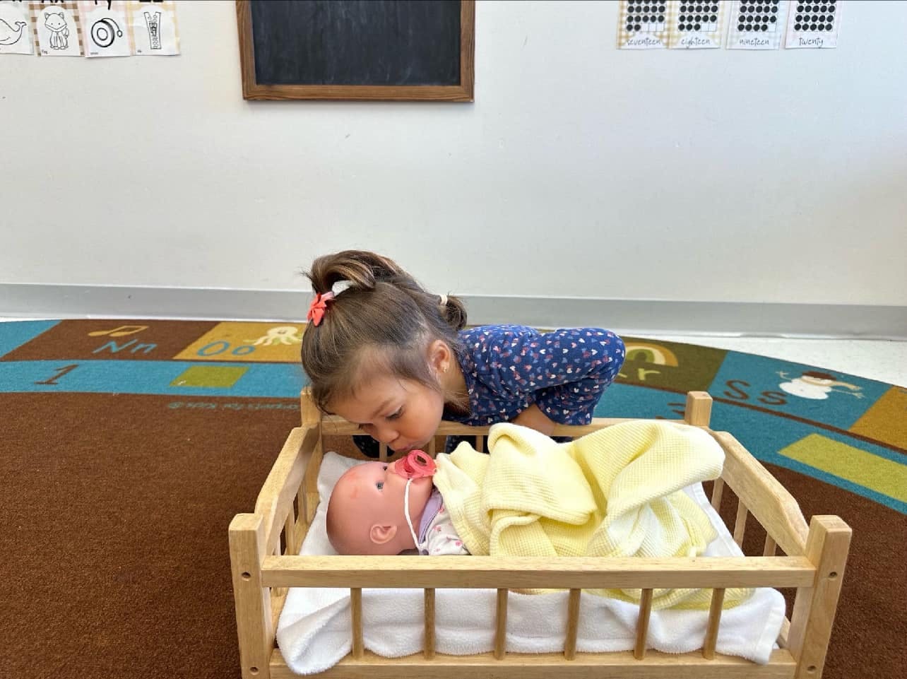 Child leaning over a doll in a wooden crib