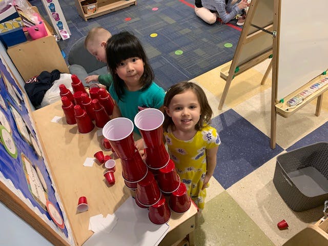 Two children standing next to stacked red cups in a classroom