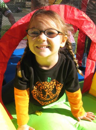 Child in glasses and pumpkin shirt in an inflatable structure