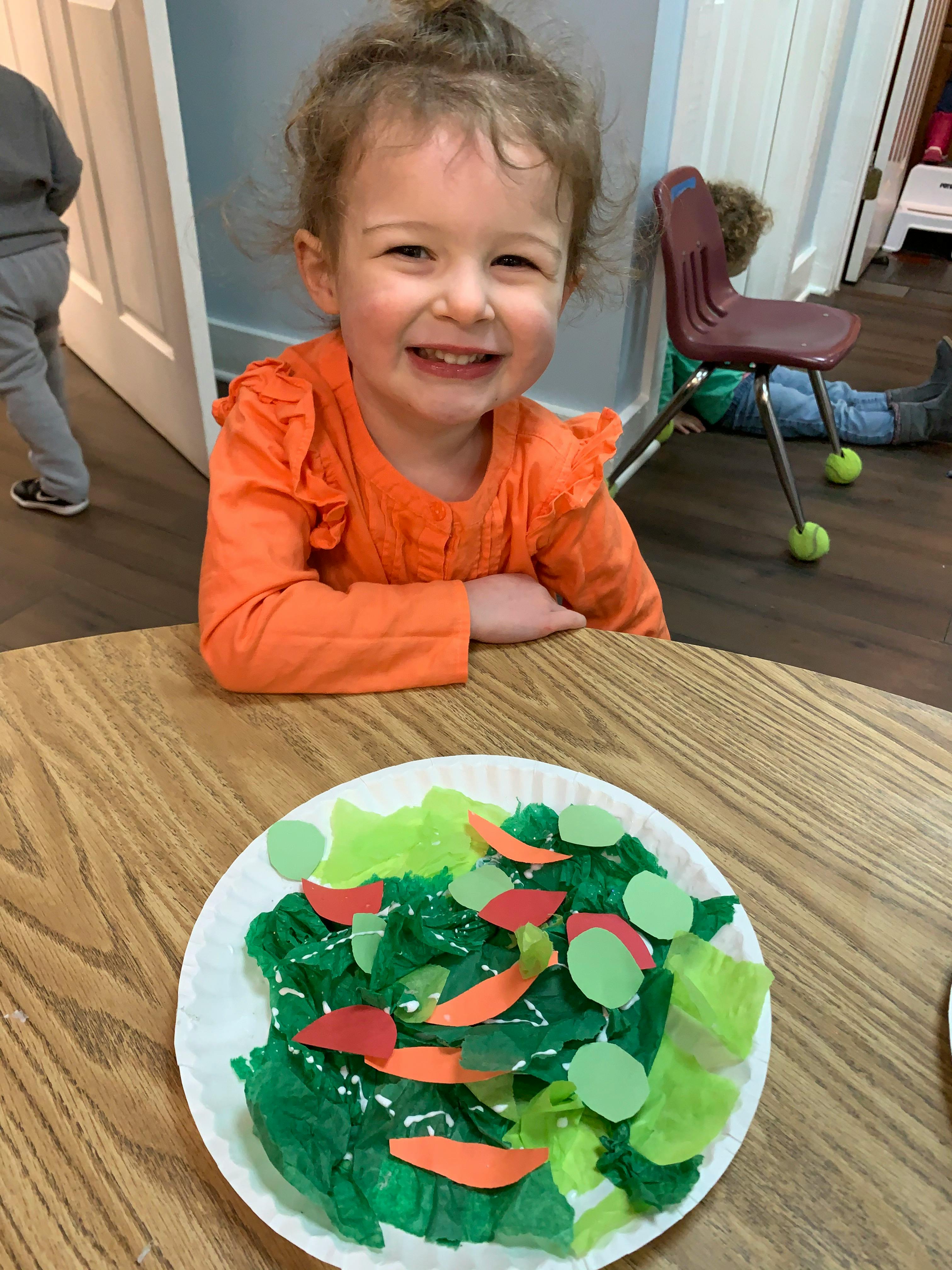 Child smiling at a table with a paper plate craft