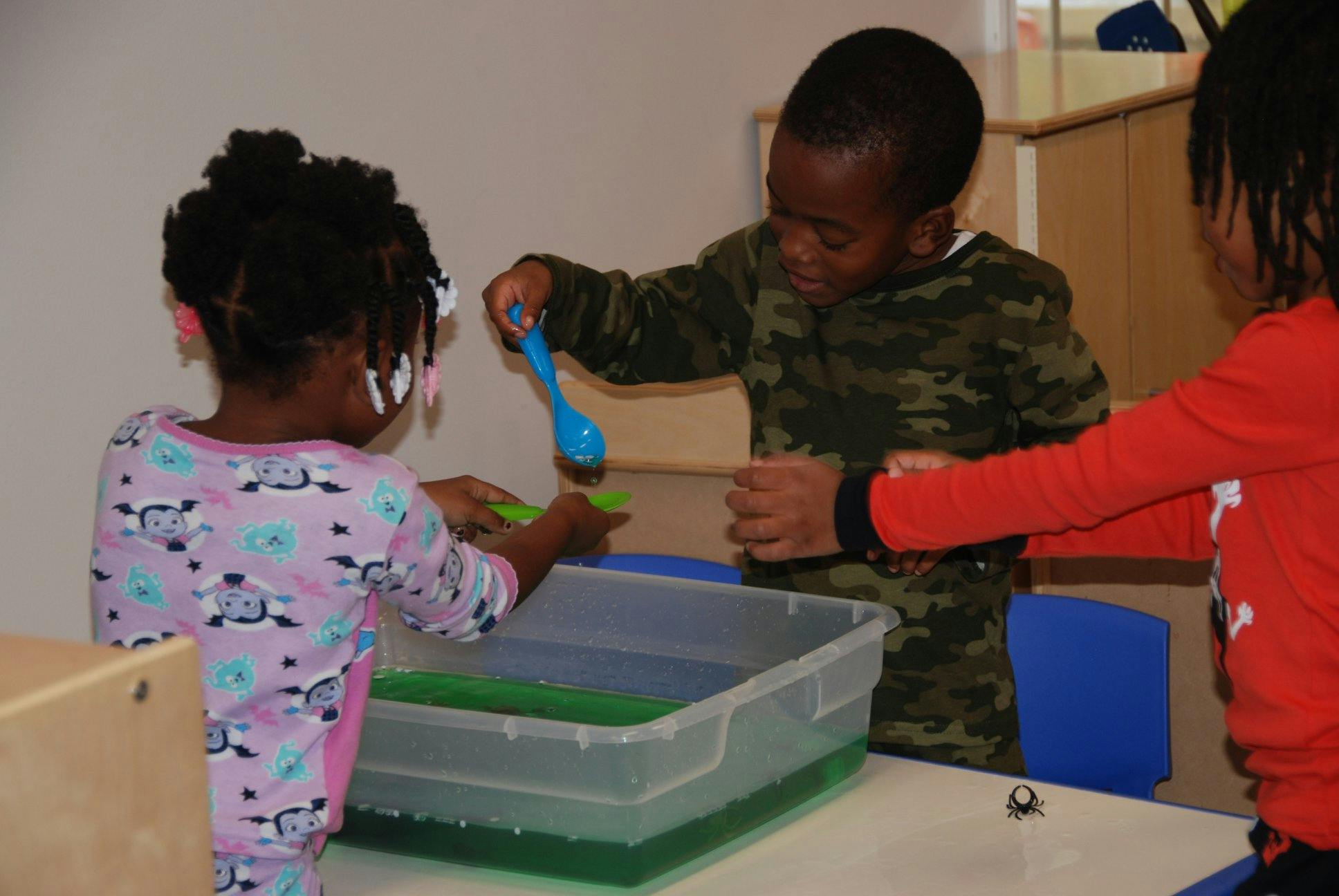 Three children playing with water and toys in a clear bin
