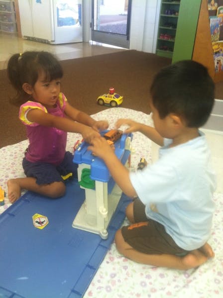 Two children playing with a toy garage and cars on the floor