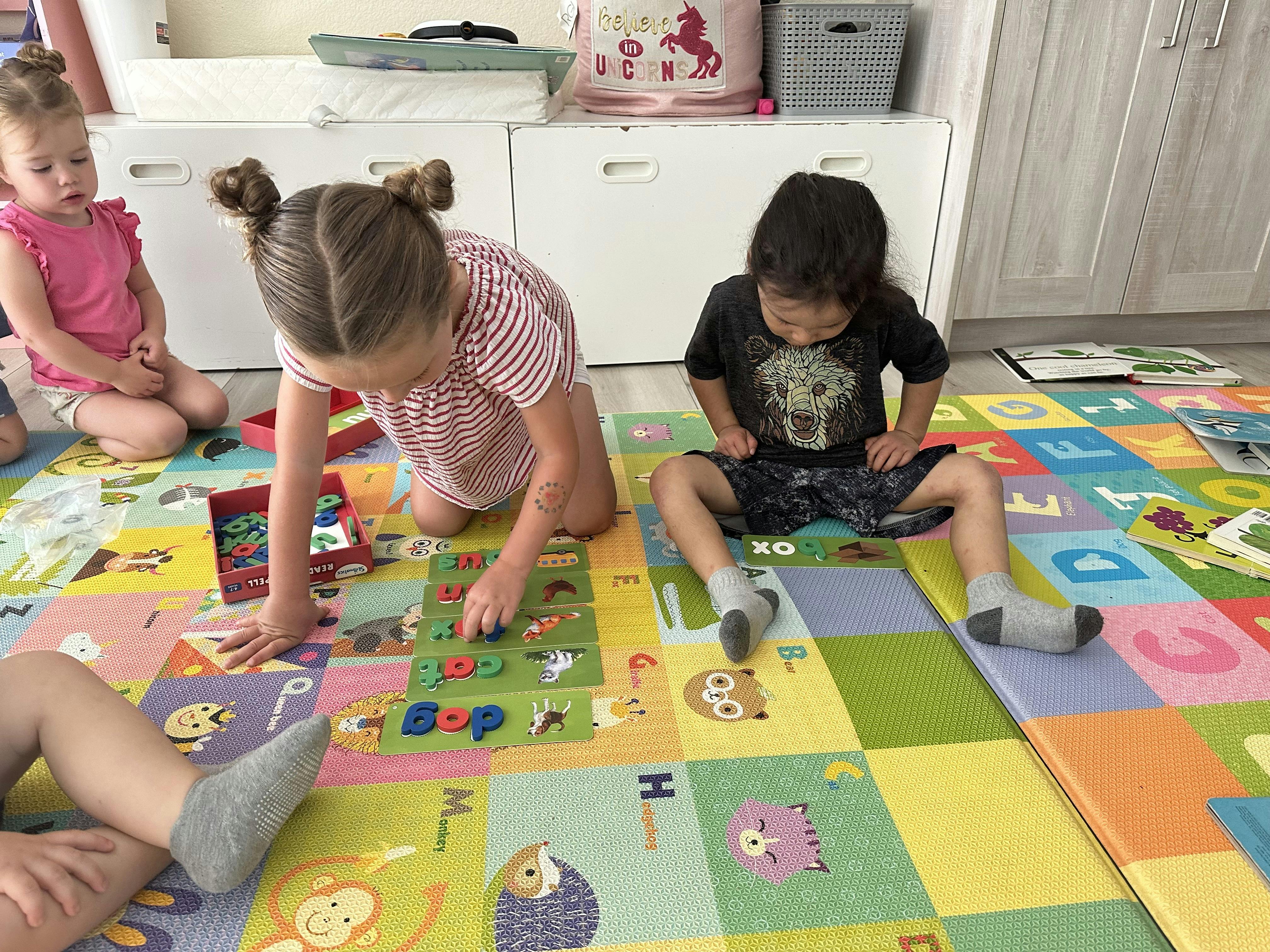 Three children playing with letter tiles on a colorful foam mat