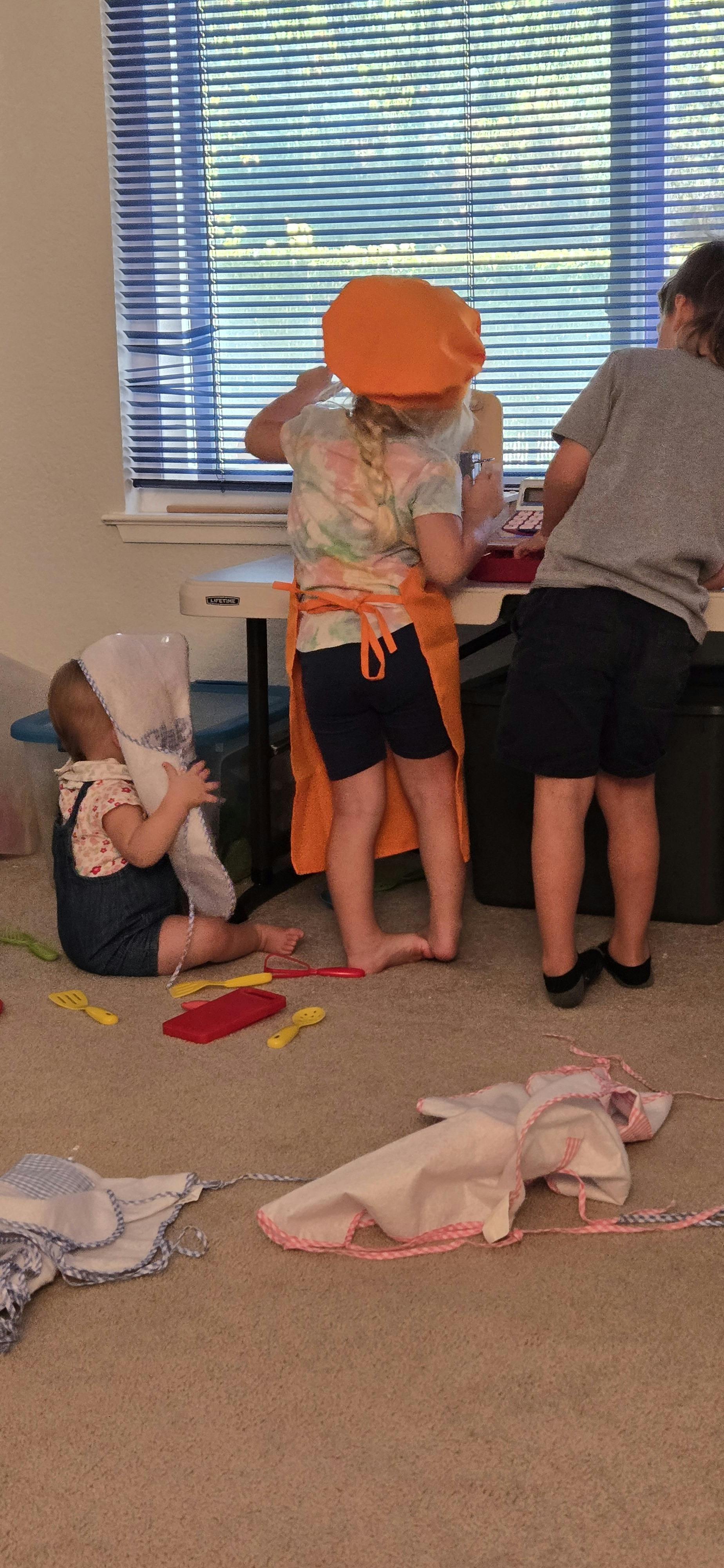 Three children playing, one wearing an apron and chef's hat