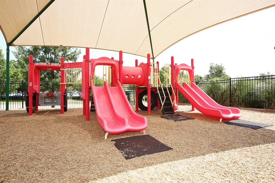 Red playground structure with slides and climbing areas under a shade canopy