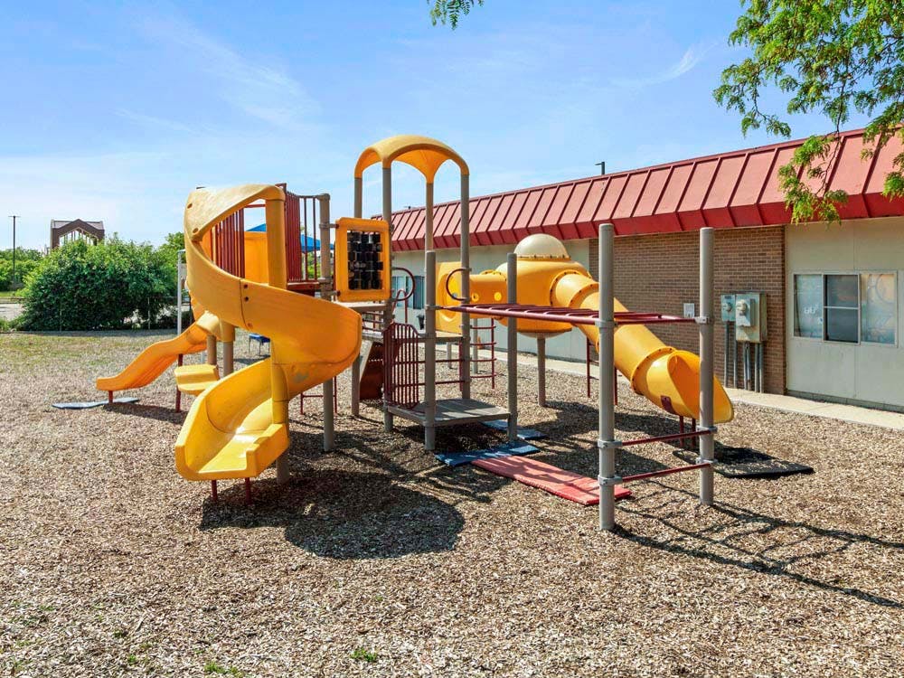 A large yellow and red playground set on wood chips next to a brick building