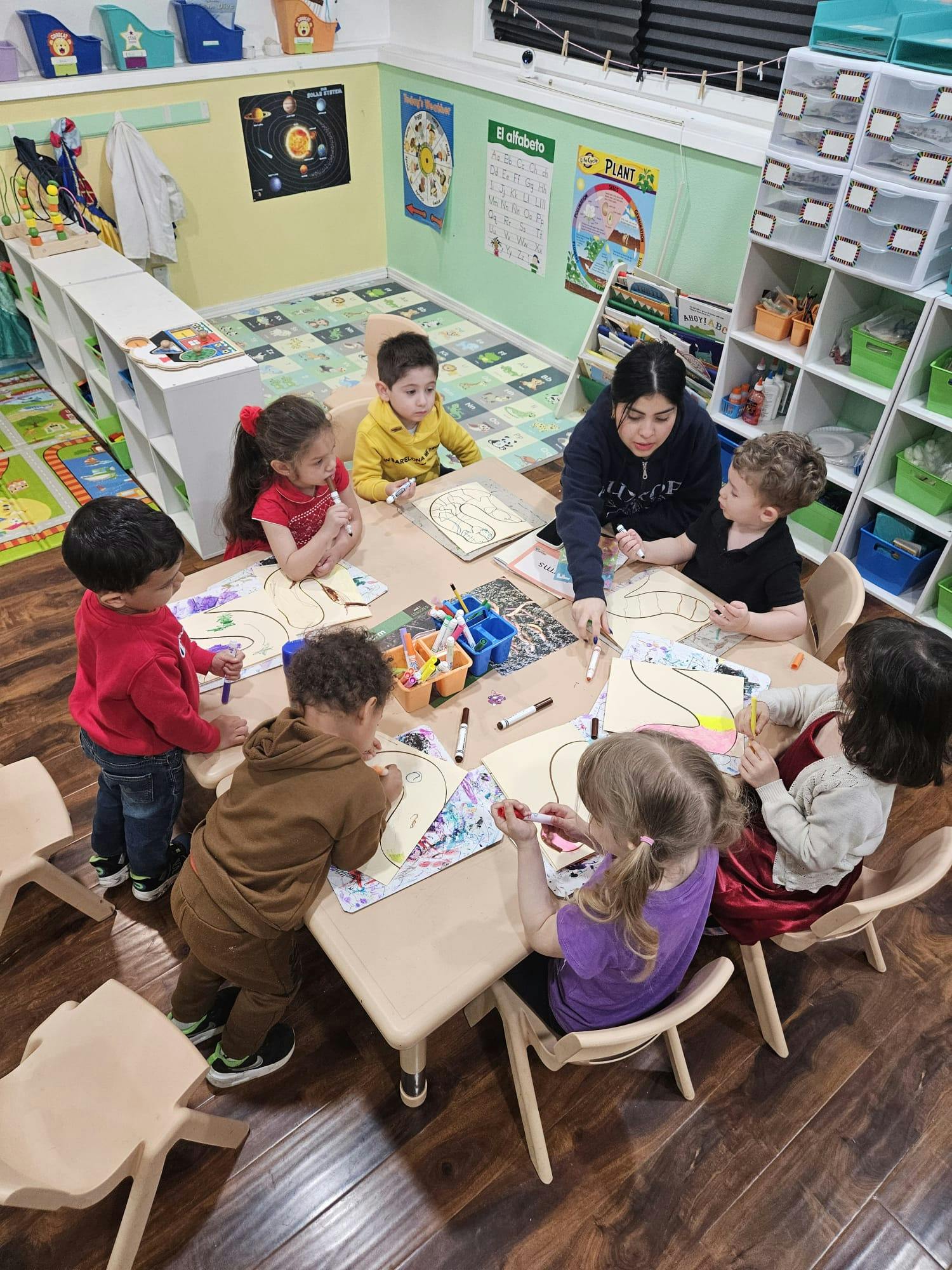 Adult and children drawing at a table in a classroom