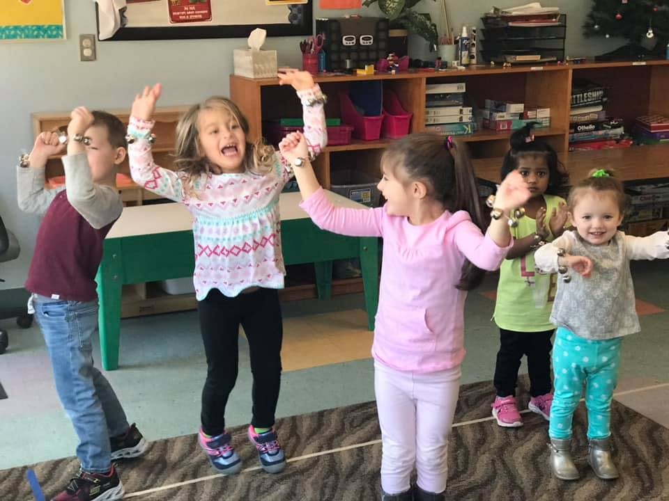 Five children with arms raised in a classroom