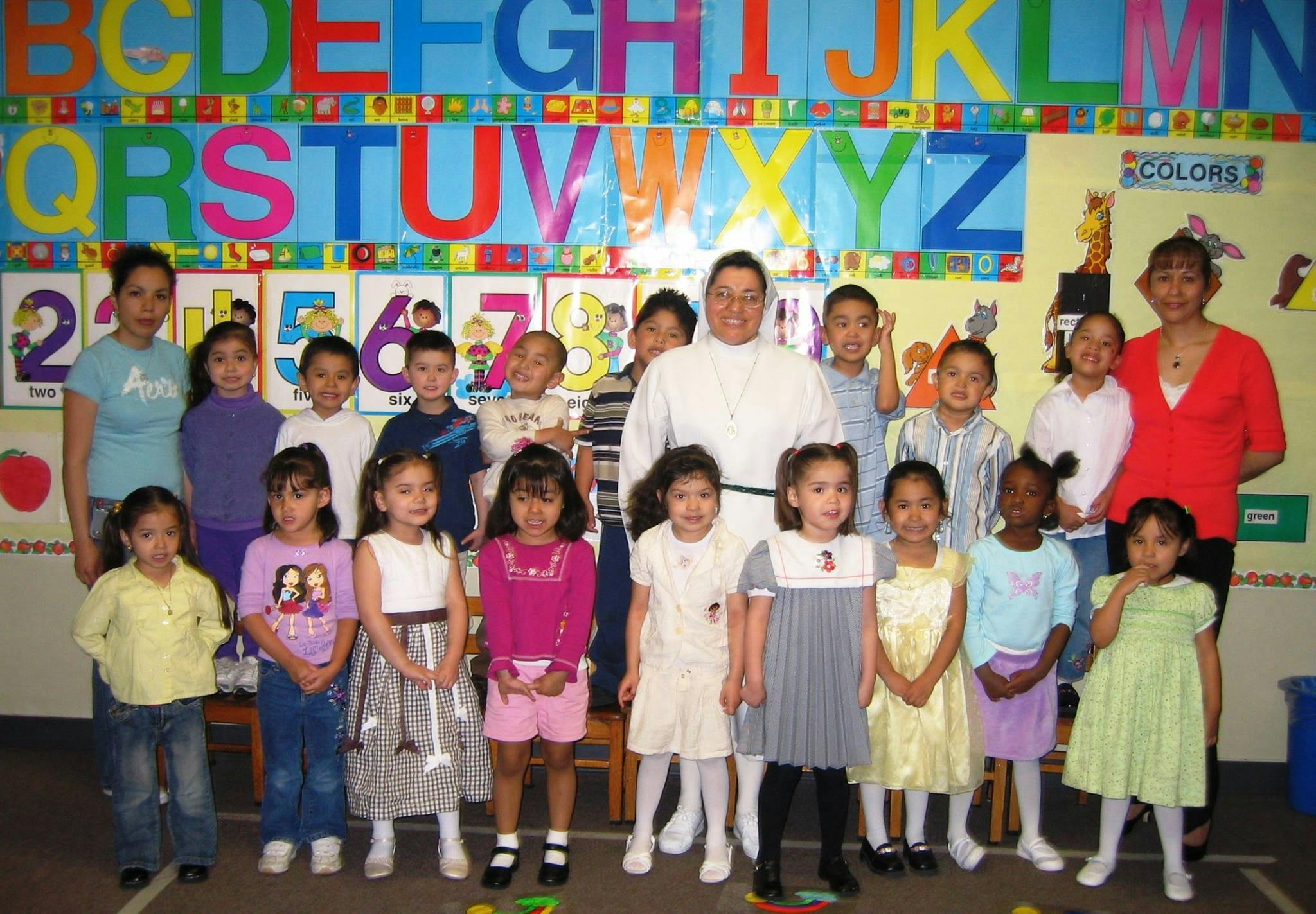 Adults and children posing in front of an alphabet chart
