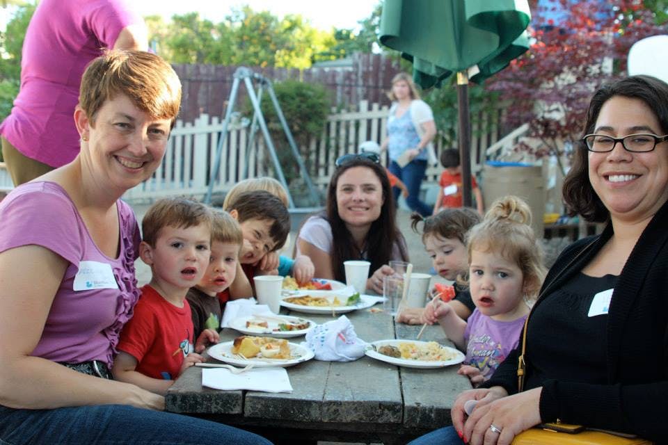 People and children eating at a picnic table outdoors