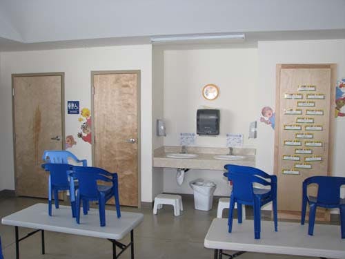 Children's bathroom with two sinks, two doors, and small blue chairs