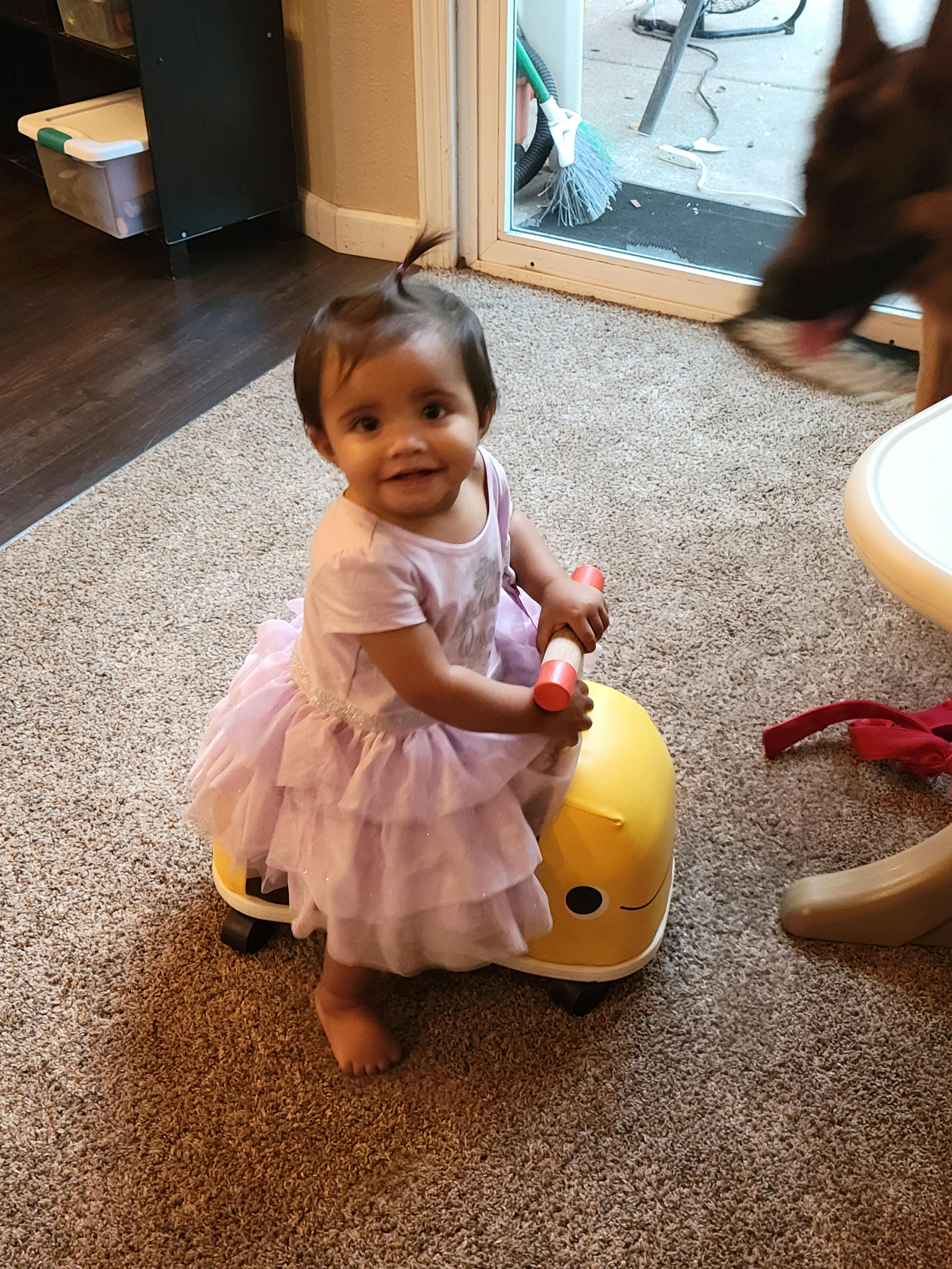 Child in a dress sitting on a yellow ride-on toy