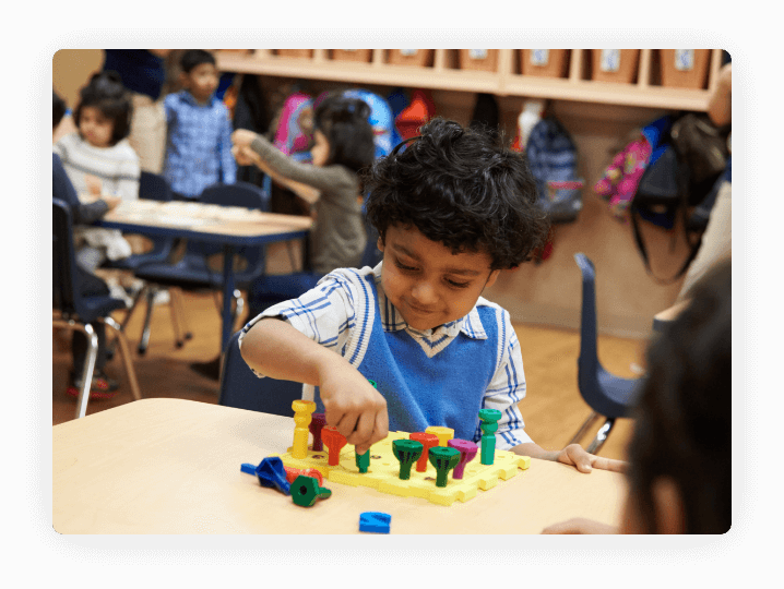 Child playing with a colorful pegboard toy at a table in a classroom