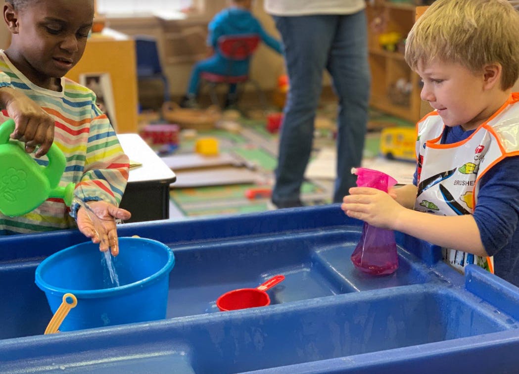 Two children playing with water in a blue sensory table