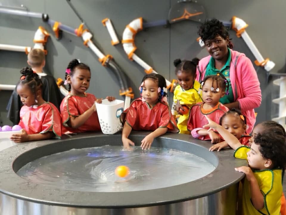 Adult and children playing with water and a ball in a sensory table